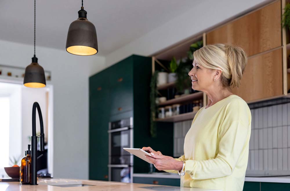 Kvinna som står i sitt kök och styr sina lampor via en padda